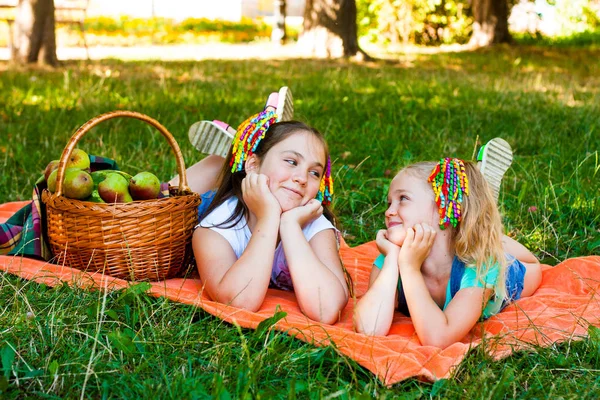 两个女孩躺在橙色的野餐毯上 公园里挂着野餐篮 — 图库照片