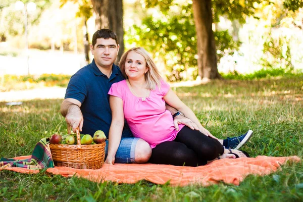 快乐的情侣们坐在橙色的野餐毯上 公园里有野餐篮 — 图库照片