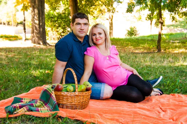 快乐的情侣们坐在橙色的野餐毯上 公园里有野餐篮 — 图库照片