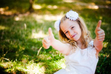 Güzel kız parkta oturur ve başparmaklarını kaldırır.