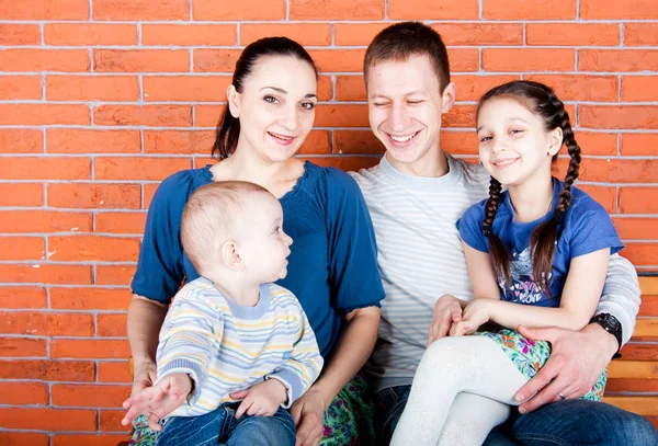 Happy family sit in  front of red bick wall. Indoor photo shot