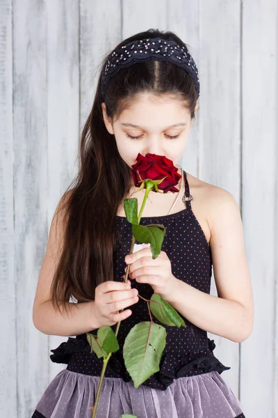 身穿黑色连衣裙的小女孩闻到红玫瑰的香味 室内摄影 — 图库照片