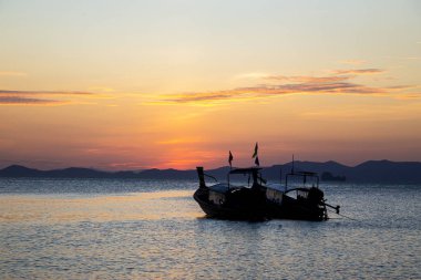 Gün batımında Khlong Muang Sahili, Krabi, Tayland 'da dalgalı denizde uzun kuyruklu tekneler..