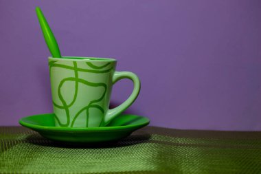 Mor arka planda çay kaşığı ile yeşil kahve fincanı