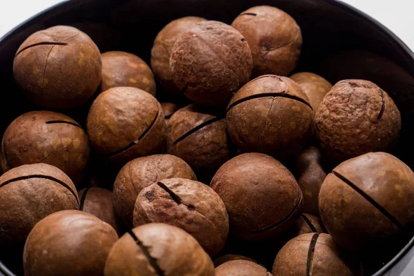 Whole macadamia nuts in black plate. Healthy vegetarian snack. Close-up photo. Vegetable diet. — 스톡 사진