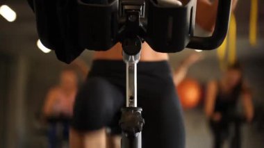 Modern karanlık bir spor salonunda spor aletleri kullanan atletik bir kız. Bisiklet pedalında spor yapmak. Kadın bacakları pedala yakın çekimde. Sağlıklı yaşam tarzı ve spor kavramları. Bisikletli kadın 