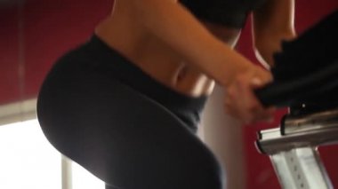 Modern karanlık bir spor salonunda spor aletleri kullanan atletik bir kız. Bisiklet pedalında spor yapmak. Kadın bacakları pedala yakın çekimde. Sağlıklı yaşam tarzı ve spor kavramları. Bisikletli kadın 