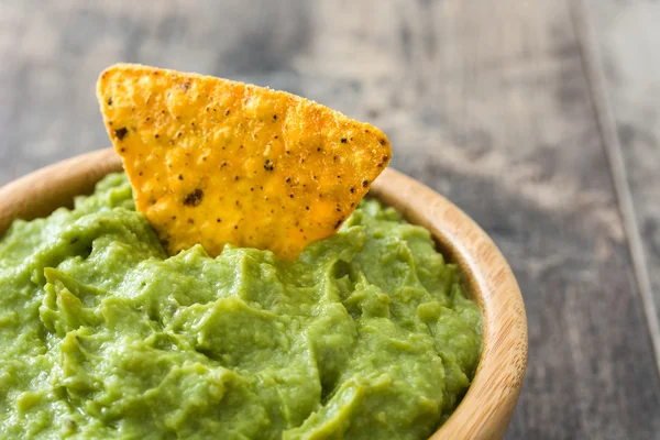 Guacamole em uma tigela e nachos em fundo de madeira — Fotografia de Stock