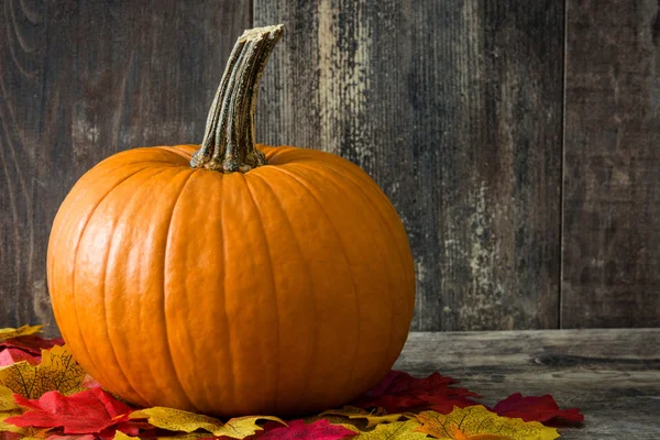 Pumpkin and autumn leaves on rustic wooden table — Stock Photo, Image