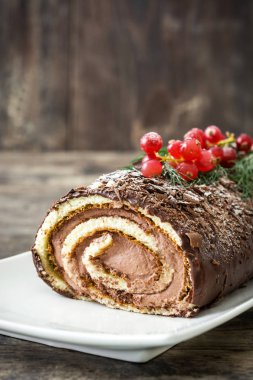 Ahşap arka plan üzerinde kırmızı kuş üzümü ile çikolata yule log pasta