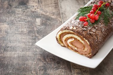 Çikolata yule log Noel Kek ile ahşap arka plan üzerinde kırmızı kuş üzümü.