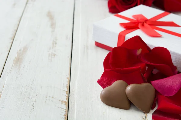 Белая подарочная коробка, конфеты и шоколад в форме сердца на деревянном столе. — стоковое фото