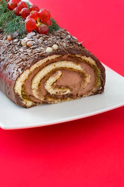 Chocolate yule log pastel de Navidad con grosella roja sobre fondo rojo — Foto de Stock