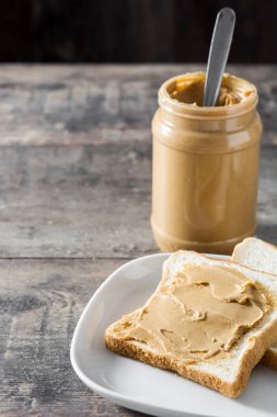 Fıstık ezmesi kavanozu ve tost ahşap masa üzerinde. Boşaltmak.