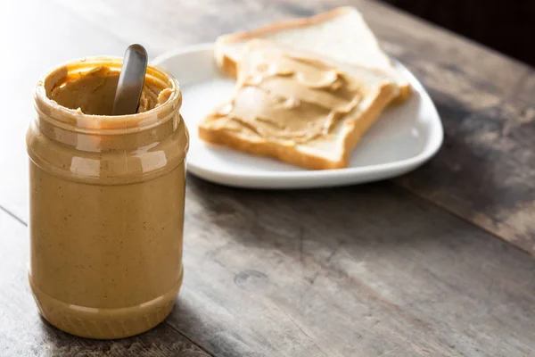 Erdnussbutter-Glas und Toastbrot auf Holztisch. Kopierraum. — Stockfoto