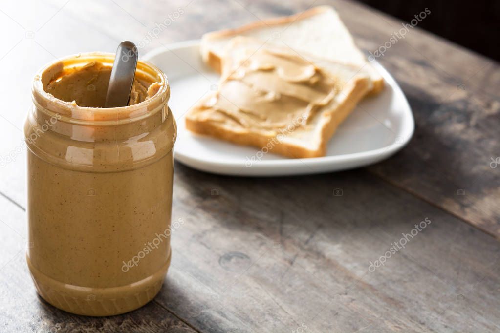 Peanut butter jar and toasts on wooden table. Copyspace.