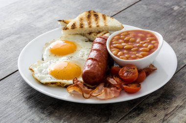 Geleneksel İngiliz kahvaltısı kızarmış yumurta, sosis, fasulye, mantar, ızgara domates ve ahşap arka planda pastırma.