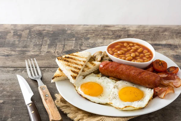 Desayuno inglés completo tradicional con huevos fritos, salchichas, frijoles, champiñones, tomates a la parrilla y tocino sobre fondo de madera. —  Fotos de Stock