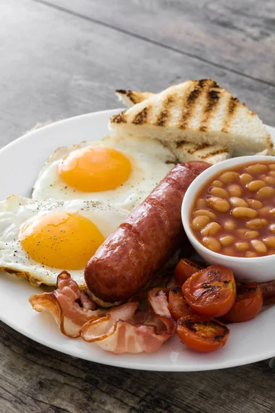 Geleneksel İngiliz kahvaltısı kızarmış yumurta, sosis, fasulye, mantar, ızgara domates ve ahşap arka planda pastırma. — Stok fotoğraf