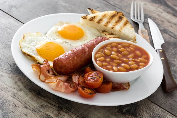 Pequeno-almoço inglês completo tradicional com ovos fritos, salsichas, feijão, cogumelos, tomates grelhados e bacon em fundo de madeira — Fotografia de Stock