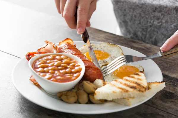 Žena jíst tradiční anglickou snídani smažená vejce, párky, fazole, houby, Grilovaná rajčata, slanina, káva a pomerančový džus, na dřevěný stůl Stock Snímky