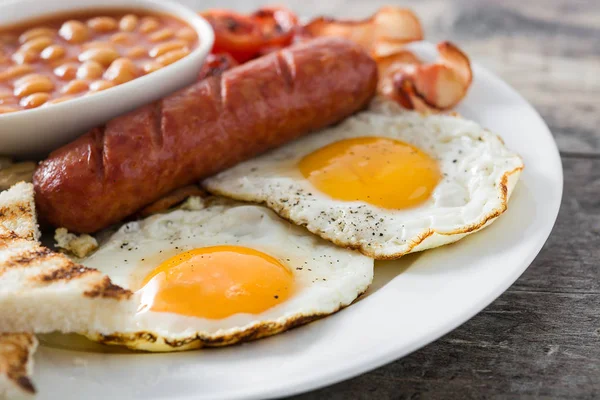 Pequeno-almoço inglês completo tradicional com ovos fritos, salsichas, feijão, cogumelos, tomates grelhados e bacon em fundo de madeira — Fotografia de Stock