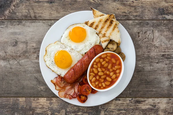 Desayuno inglés completo tradicional con huevos fritos, salchichas, frijoles, champiñones, tomates a la parrilla y tocino sobre fondo de madera. —  Fotos de Stock