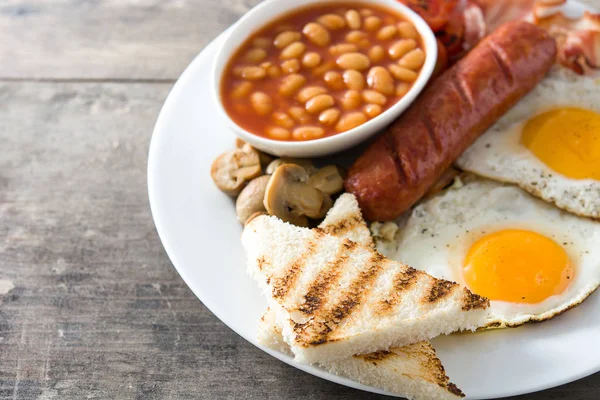 Традиційний англійський сніданок з смаженими яйцями, ковбасою, квасолею, грибами, смаженими помідорами і беконом на дерев "яному тлі. — стокове фото