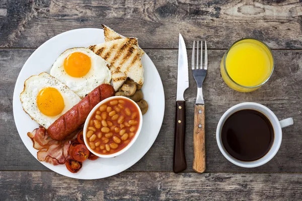 Pequeno-almoço inglês completo tradicional com ovos fritos, salsichas, feijões, cogumelos, tomates grelhados e bacon no fundo de madeira.Vista superior — Fotografia de Stock