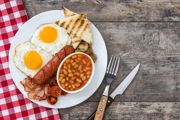 Παραδοσιακό πλήρες αγγλικό πρωινό με τηγανητά αυγά, λουκάνικα, φασόλια, μανιτάρια, ψητή ντομάτα και μπέικον σε ξύλινο πλαίσιο. Το Top view — Φωτογραφία Αρχείου