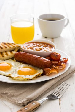 Geleneksel İngiliz kahvaltısı kızarmış yumurta, sosis, fasulye, mantar, ızgara domates ve ahşap arka planda pastırma.