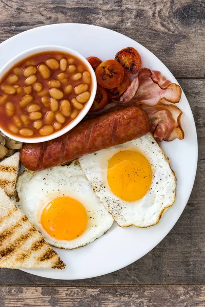 Petit déjeuner anglais traditionnel complet avec œufs frits, saucisses, haricots, champignons, tomates grillées et bacon sur fond de bois — Photo