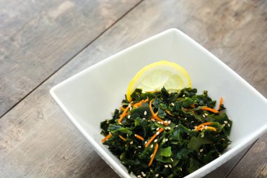 WAKAME salata havuç, susam ve ahşap masa üzerinde bir kapta limon suyu ile