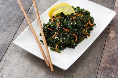 WAKAME salata havuç, susam ve platel ahşap masa üzerinde limon suyu ile