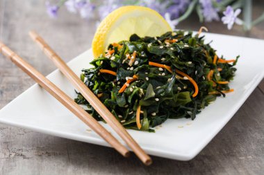 WAKAME salata havuç, susam ve platel ahşap masa üzerinde limon suyu ile