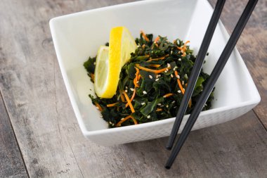 WAKAME salata havuç, susam ve ahşap masa üzerinde bir kapta limon suyu ile