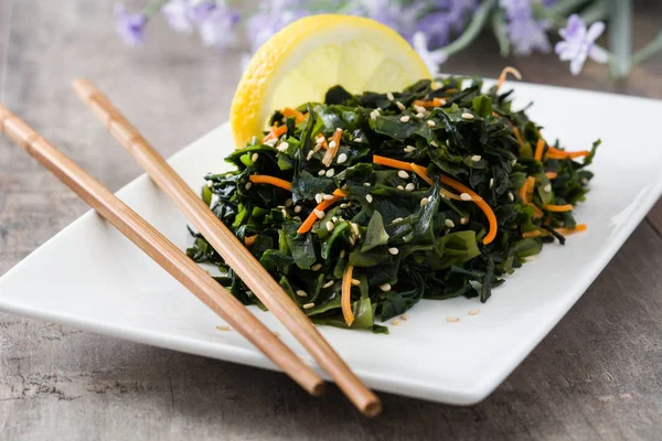 Wakame salad with carrot, sesame seeds and lemon juice in platel on wooden table — Stock Photo, Image