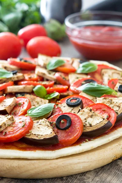 Vegetarian pizza with eggplant, tomato, black olives, oregano and basil on wooden background — Stock Photo, Image