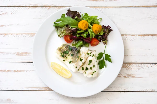 Ikan kod goreng dan salad di piring dengan latar belakang kayu putih — Stok Foto