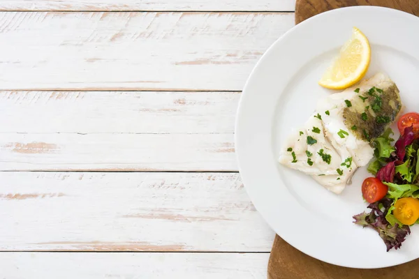 Filete de bacalao frito y ensalada en plato sobre fondo de madera blanca — Foto de Stock