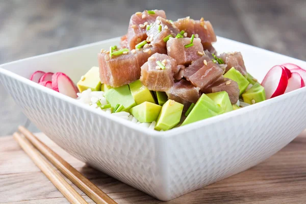 Hawaiian tuna poke bowl with avocado, radishes and sesame seeds on wooden background
