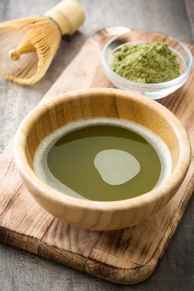 Matcha chá verde em uma tigela e batedor de bambu, em fundo de madeira — Fotografia de Stock