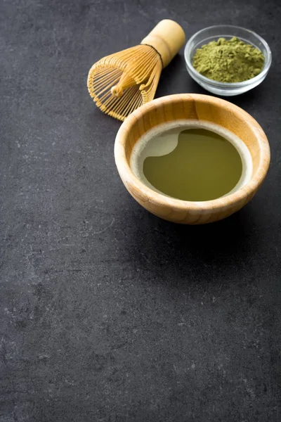 Matcha chá verde em uma tigela e batedor de bambu na ardósia preta — Fotografia de Stock