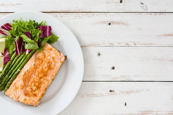 Filete de salmón a la parrilla con espárragos y ensalada en plato sobre mesa de madera blanca — Foto de Stock