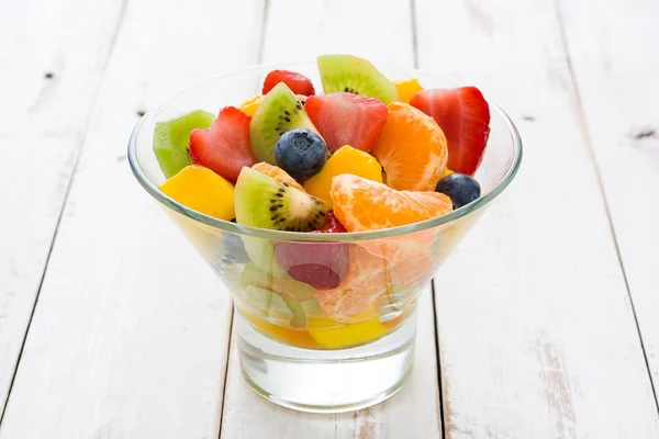 Fruit salad in crystal bowl on white wooden table.