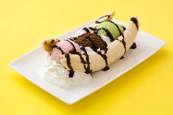 Sobremesa de sorvete banana split com xarope de chocolate em fundo amarelo — Fotografia de Stock