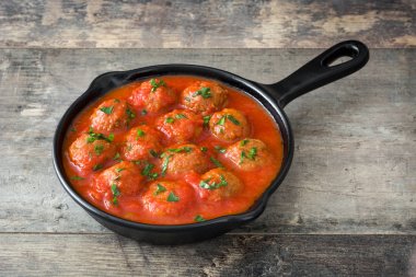 Meatballs with tomato sauce in iron frying pan on wooden table clipart