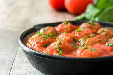 Meatballs with tomato sauce in iron frying pan on wooden table clipart