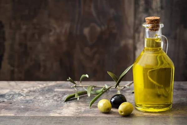 Aceite de oliva virgen en una botella de cristal sobre fondo de madera — Foto de Stock
