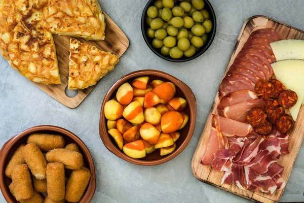 Tapas tradicionales españolas. Croquetas, aceitunas, tortillas, jamón y patatas bravas sobre piedra gris — Foto de Stock